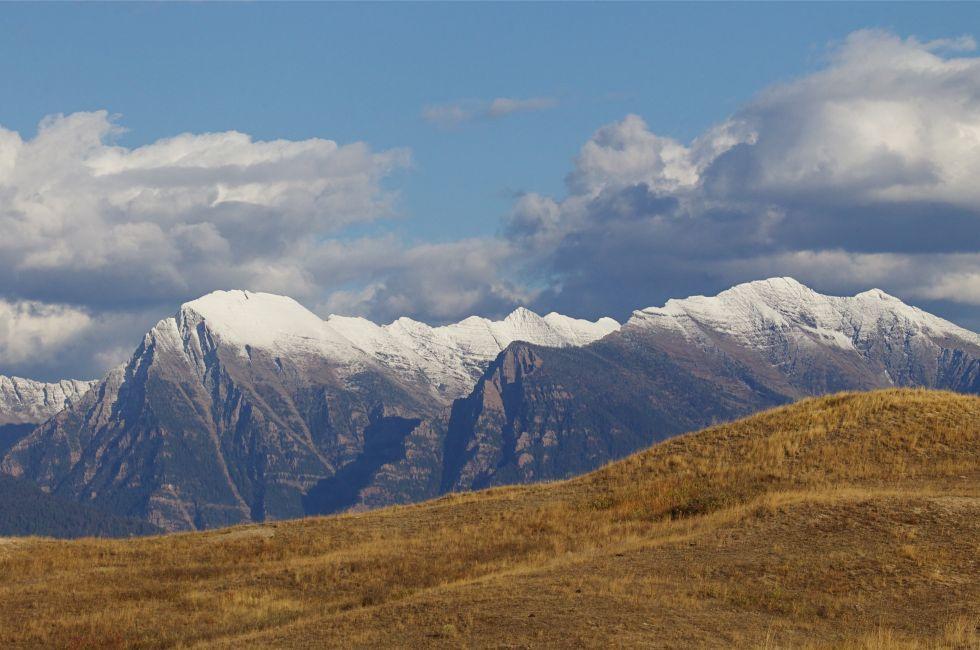 The Rocky Mountains of Montana Mission Mountain Range between Missoula and Kalispel with snow capped peaks, blue sky with clouds, and prairie grass lands, on the Flathead Indian Reservation