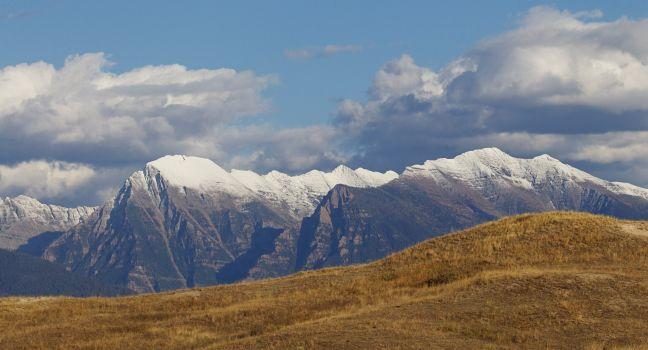 The Rocky Mountains of Montana Mission Mountain Range between Missoula and Kalispel with snow capped peaks, blue sky with clouds, and prairie grass lands, on the Flathead Indian Reservation