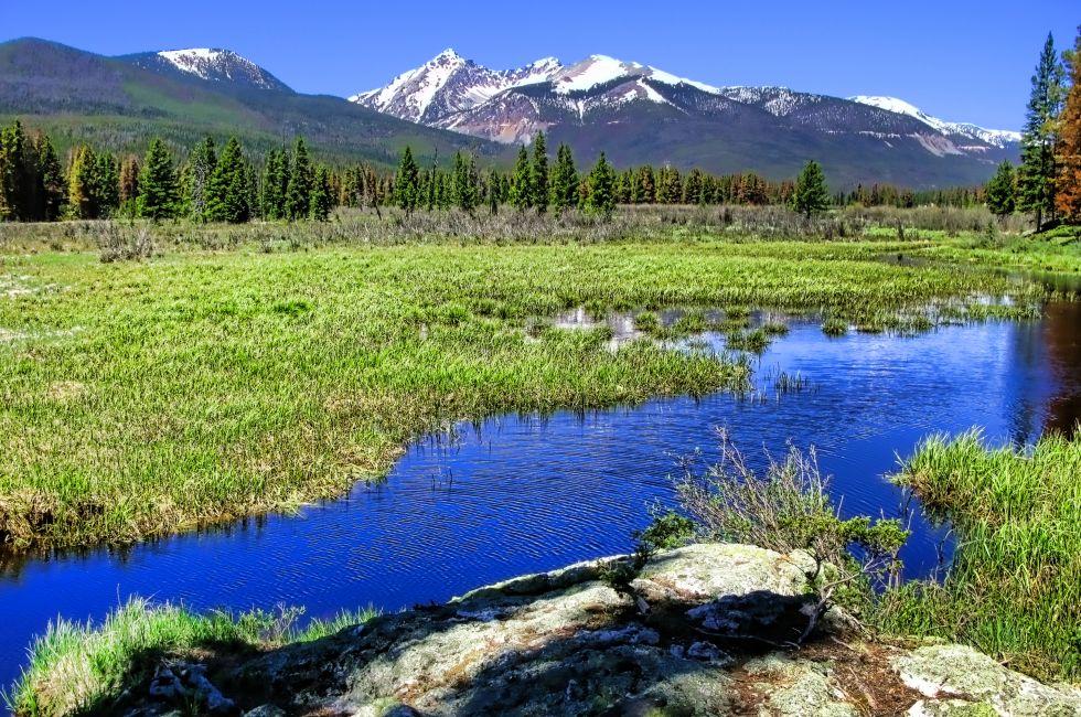 Rocky Mountains National Park scenic panorama landscape with river meandering through an alpine meadow and snow covered high mountain peaks in the distance in Colorado