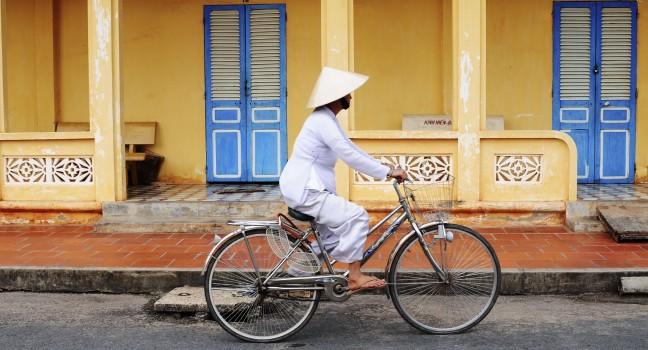 Asian woman with conical hat, riding bike on street in Tay Ninh province, Vietnam.; 