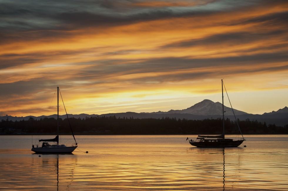 A sailboat anchors off of Lummi island, located in the San Juan Islands of the Puget Sound area of western Washington state. The volcano,Mt. Baker, can be seen in the background.