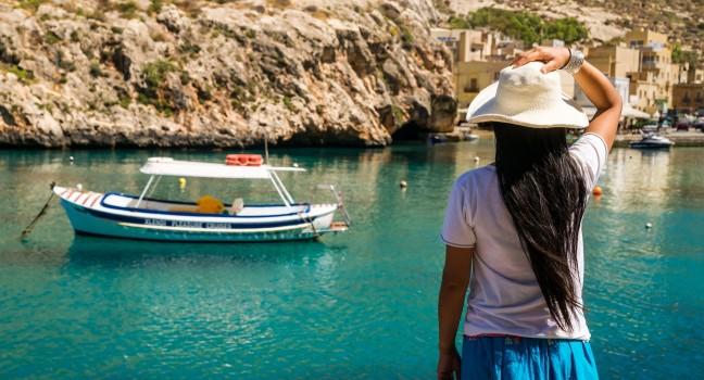 An asian lady enjoys the view over the waters of Xlendi Bay at Gozo Island, part of the maltese archipel; 