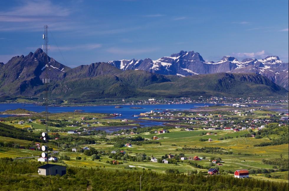 Scenic panorama with green meadows, town of Leknes and snowy peaks of picturesque Lofoten islands in Norway; 